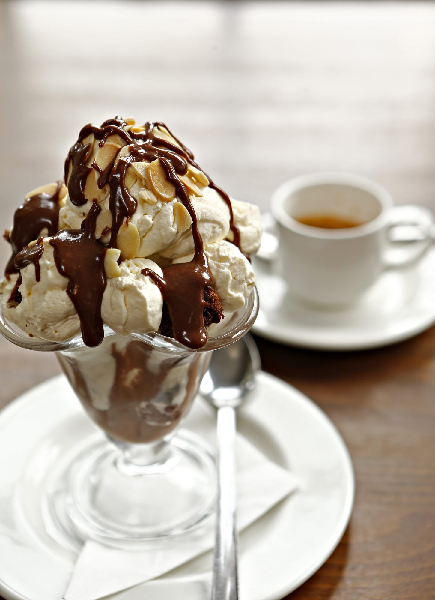 Ice cream sundae with chocolate sauce beside cup of coffee